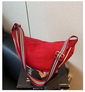 Detail of red crescent canvas bag with adjustable striped shoulder strap and top zipper