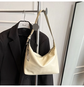Détail du sac sous le bras en cuir beige avec un pendentif en métal argenté en cœur