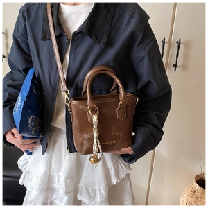 Detail of a brown leather bucket bag with gold logo and silk scarf charm on the handle