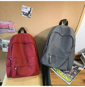 Minimalist waterproof nylon backpacks in burgundy and dark grey on a wooden desk