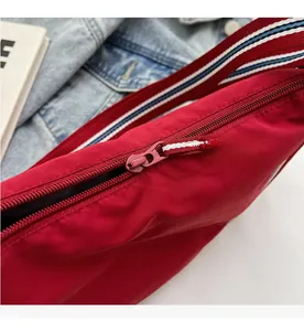 Detail of smooth red zipper and tricolor striped strap on a nylon dumpling bag