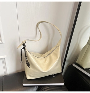 Detail of cream white faux leather shoulder bag featuring a black heart charm on book