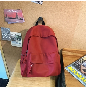 Detail of red nylon backpack on wooden table featuring large main pocket and front zipper