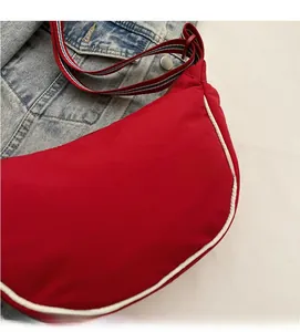 Detail of red crescent nylon bag with contrast piping and striped woven shoulder strap