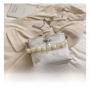 Détail du sac seau en satin blanc avec broderie florale et accents de chaîne en perles