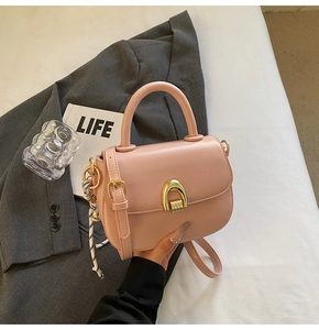 Detail of light pink saddle bag featuring a smooth leather finish and gold U-shaped buckle