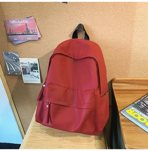 Detail view of brick red canvas backpack with large front zipper pocket and strap