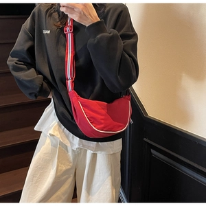 Detail of red crescent canvas bag with striped strap shown in a street style view