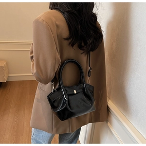 Dettaglio di una borsa tote nera lucida che mostra la trama a pieghe e la tracolla sottile