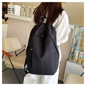 Detail of black backpack with herringbone texture and adjustable straps shown on a model