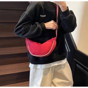 Detail of red crescent shoulder bag with white piping and striped strap on model