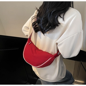 Close-up of red crescent canvas bag with striped shoulder strap and white piping detail