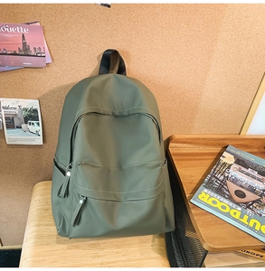 Olive green nylon backpack with multiple compartments placed on a wooden bench