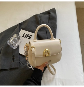 Detail of cream saddle bag with golden horseshoe clasp and decorative silk scarf