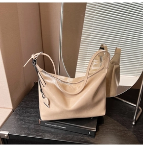 Détail du sac hobo beige brillant avec nœud tressé et pendentif cœur en argent
