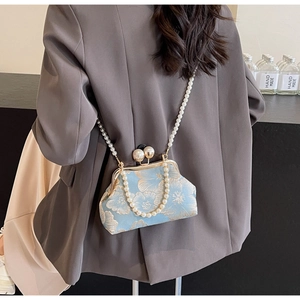 Detail of blue embroidered bag with pearl straps and golden floral pattern on grey suit