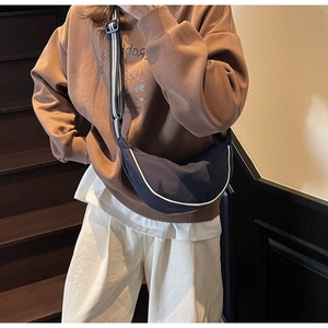 Detail of dark blue crescent canvas bag featuring contrast white piping and striped strap