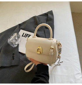 Close-up of a beige saddle bag with a golden metal arch buckle and braided charm detail