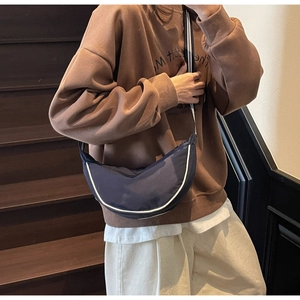 Detail of navy crescent crossbody bag with white piping and striped strap on model