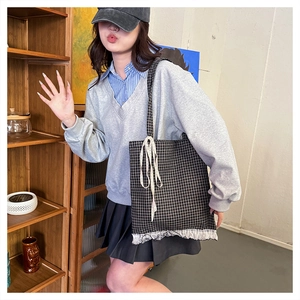 Detail of checkered tote bag featuring white lace trim and bow knot on the shoulder strap
