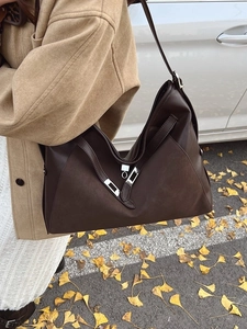 Deep brown leather tote bag with silver buckle worn by a woman in camel coat