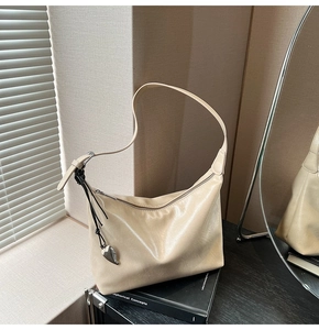 Détail d'un sac porté épaule beige avec breloque cœur et sangle tissée noire
