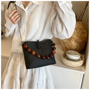 Détail du sac bandoulière noir avec perles d'ambre, chaîne et nœud chinois décoratif