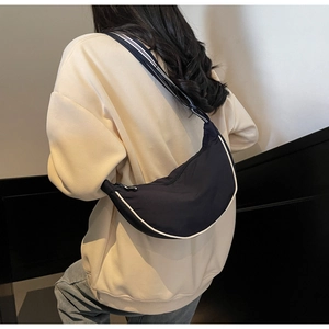 Detail of navy nylon crescent bag with contrast white piping and striped shoulder strap