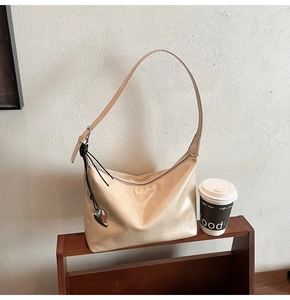 Détail du sac cabas en cuir verni beige avec un pendentif en forme de cœur argenté sur l'anse