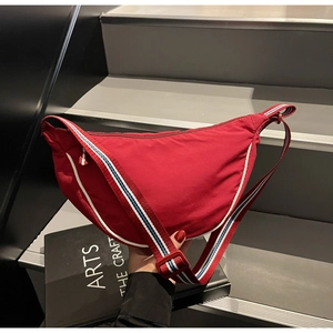 Close-up of red crescent canvas bag with tricolor striped strap on minimalist steps