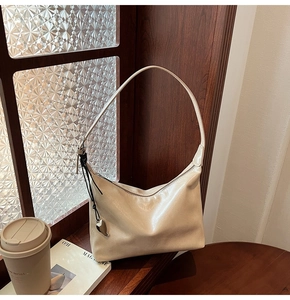 Détail du sac à bandoulière beige avec texture en cuir lisse et pendentif en forme de cœur