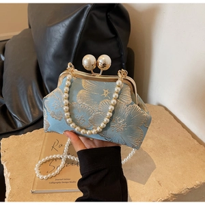 Close-up of vintage blue floral embroidery with gold frame and large pearl clasp
