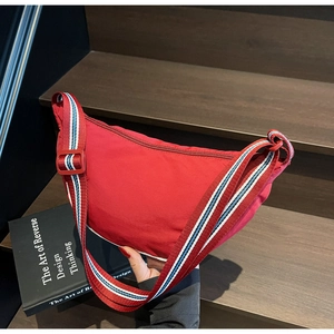 Detail of red crescent canvas bag with striped adjustable strap on a wooden step