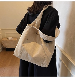 Detail of beige corduroy tote bag showing metal rivets and soft ribbed texture on shoulder