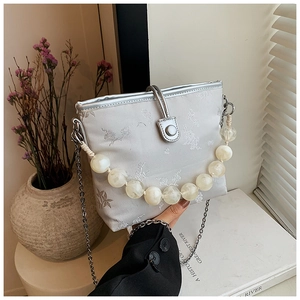 Détail du sac seau argenté brodé de fleurs avec anse en perles et bandoulière