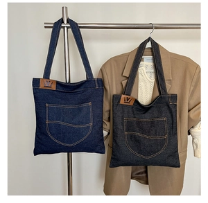 Detail of denim tote bags in dark blue and black featuring wavy pockets and leather logo