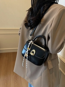 Black leather saddle bag with gold horseshoe buckle and striped silk scarf wrap handle