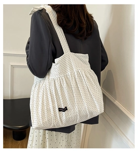Detailed side view of white polka dot tote bag with pleated texture on female model