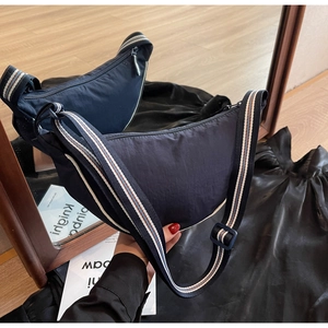 Detail of dark blue crescent crossbody bag featuring a striped shoulder strap and zip closure