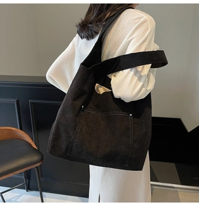Detail of black corduroy tote bag showing thick ribbed texture and front pocket design