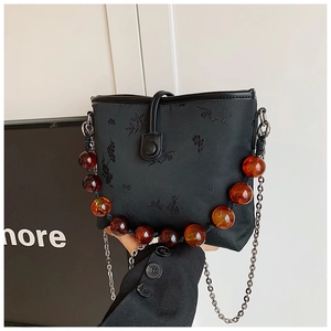 Détail de broderie florale sur sac seau en satin noir avec chaîne perlée ambrée