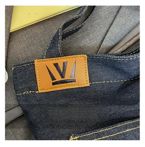 Detail of dark blue denim tote with contrast yellow stitching and brown leather patch