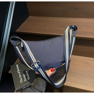Detail of navy blue crescent nylon bag with striped strap on wooden stairs