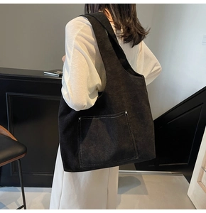 Detail of black corduroy tote bag showing front pocket with contrast white stitching