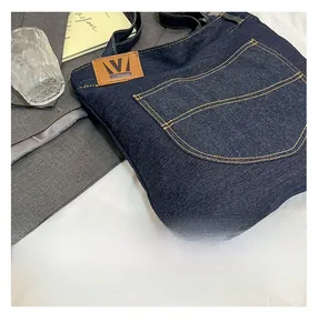 Detail of dark blue denim tote bag with leather logo patch and jeans style pocket stitching