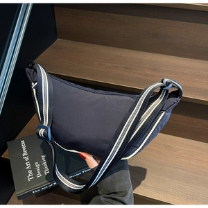 Close-up of dark blue nylon crescent bag with striped adjustable shoulder strap on stairs