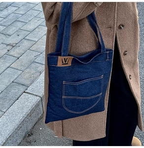 Detail of a large dark blue denim tote bag with external pocket and leather patch on street