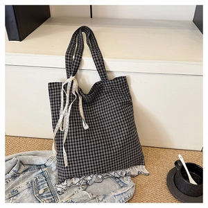 Detail of checkered tote bag featuring white lace trim and ribbon on white display stand