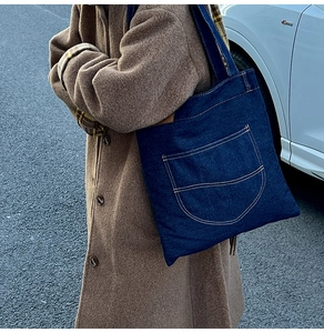 Outdoor lifestyle shot of a large denim tote bag featuring contrast orange stitching details