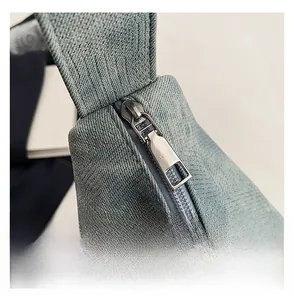 Close-up of smooth silver metal zipper on light blue denim hobo shoulder bag texture